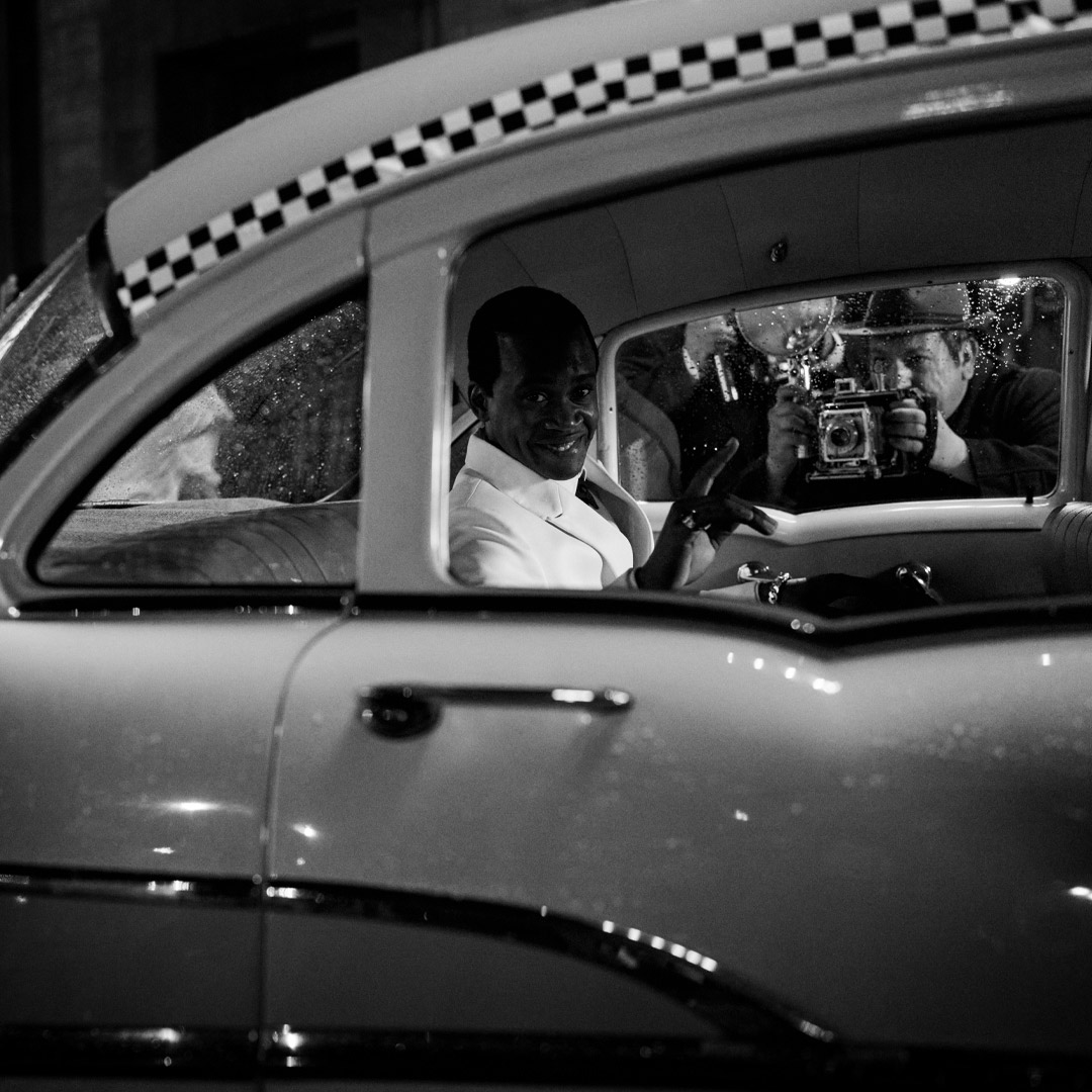 Grayscale photo of same musician sitting in a car